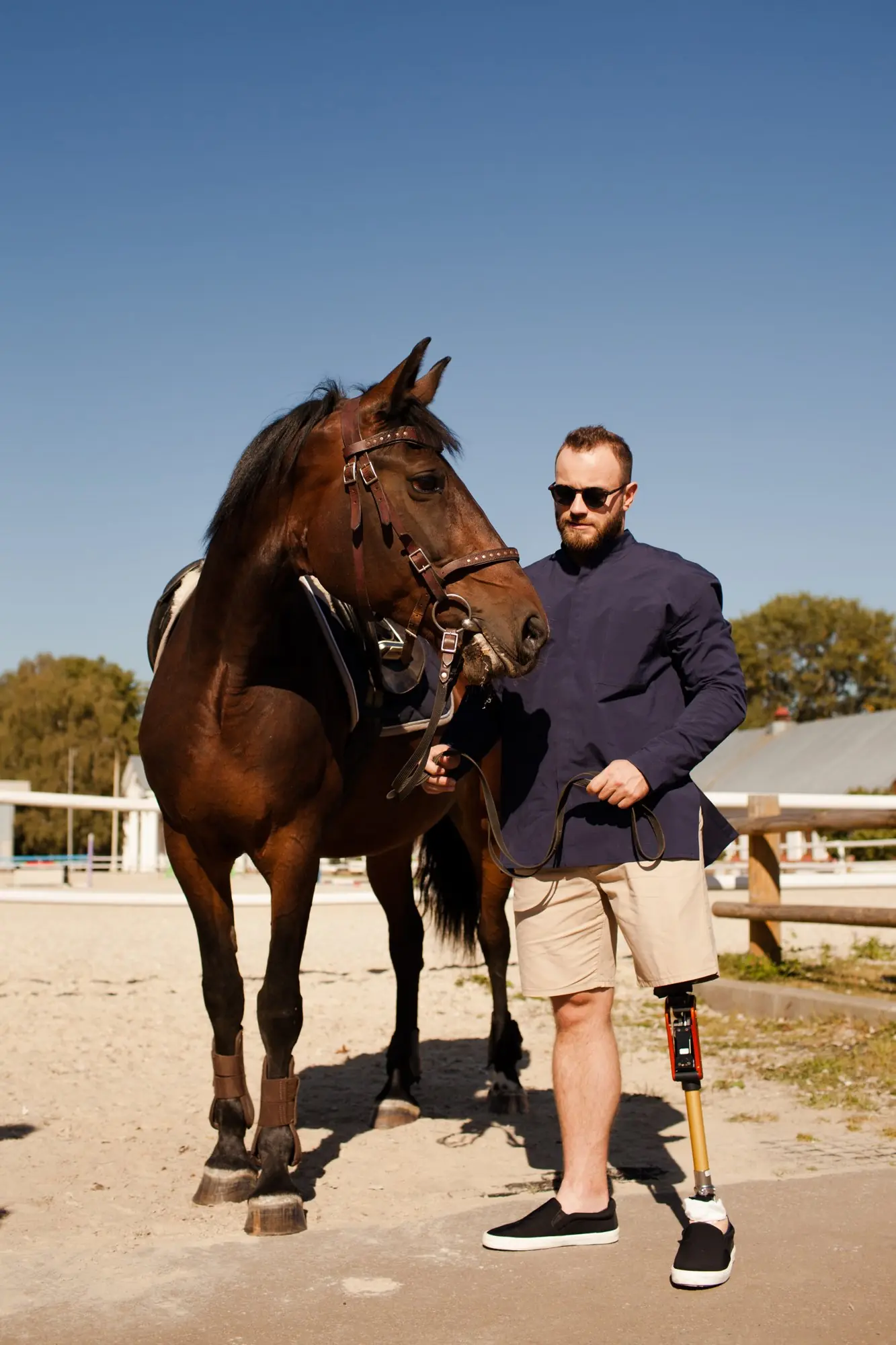 Hombre con prótesis de pierna sosteniendo un caballo por las riendas