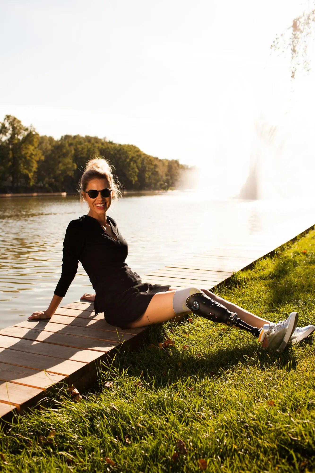 Mujer sentada en un deck a la orilla del lago, con prótesis de pierna